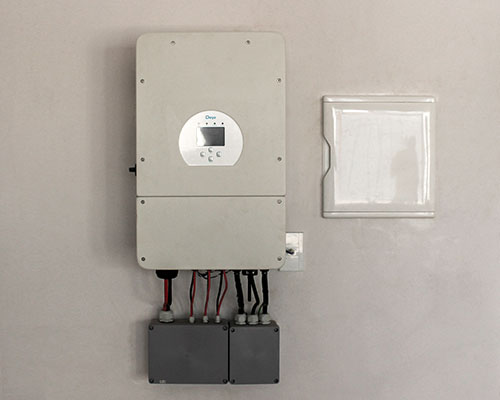 Imagem de um inversor híbrido de energia solar instalado na parede, com cabos conectados na parte inferior, utilizado para gerar energia solar em residências.