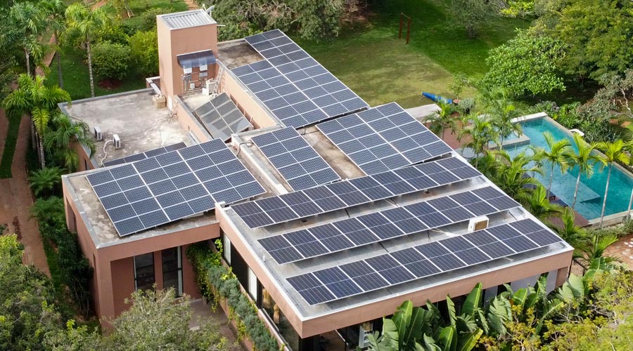 Residência de alto padrão com painéis solares instalados no telhado, cercado por vegetação e área de lazer com piscina ao fundo. Projeto aprovado pela CEMIG e desenvolvido pela Sunus em Brumadinho - MG.