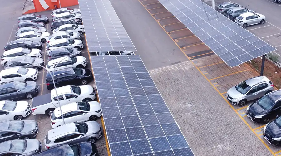 Carros estacionados em vagas de supermercado que contam com painéis solares (carports), proporcionando sombra e geração de energia.